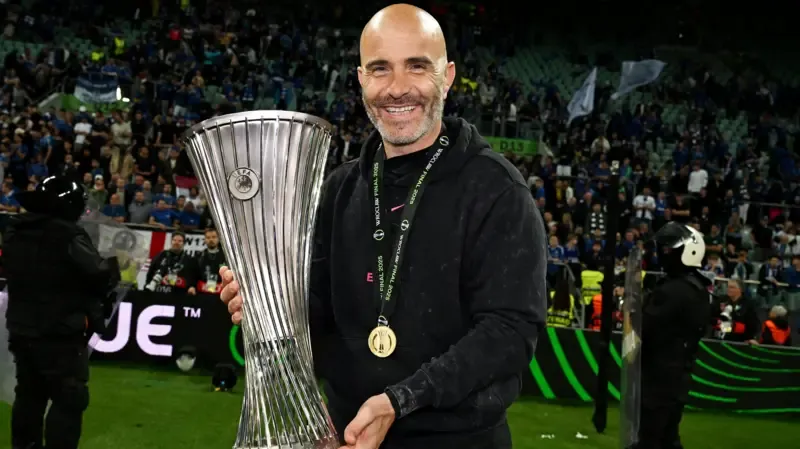 Enzo Maresca with the Europa Conference League trophy. He is wearing a gold medal and a black jumper.